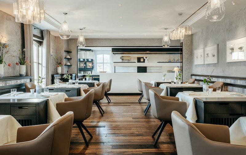 Modernes Restaurant: braune Stühle, weiße Tischdecken, Holzböden, hell.