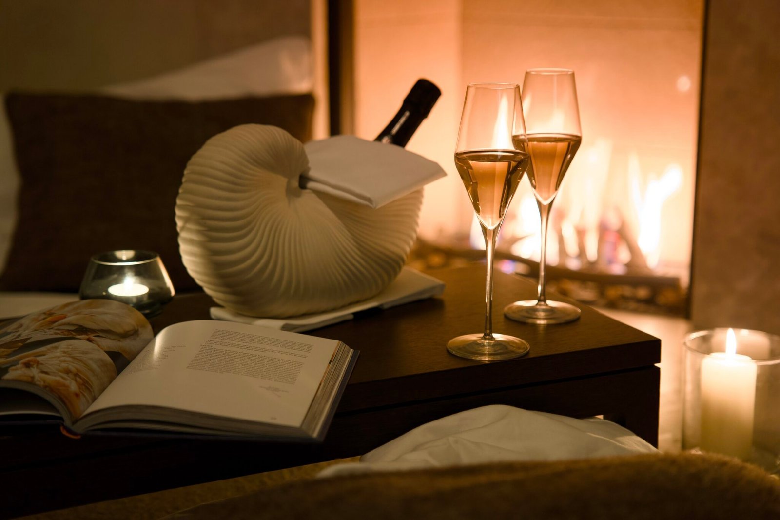 Warmes, gemütliches Zimmer: Sektgläser, Flasche, Buch, Kerze, Kamin.