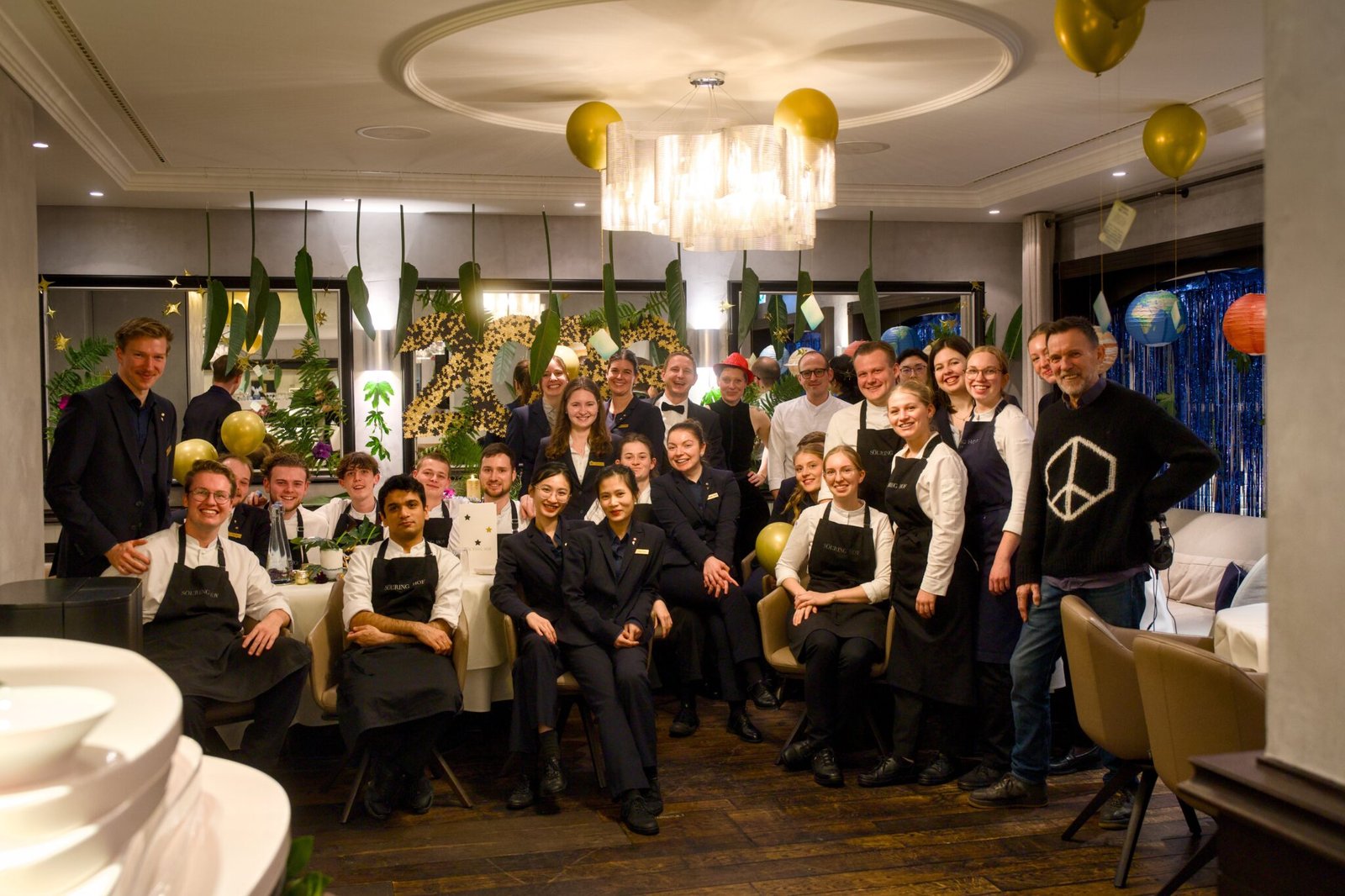 Restaurantmitarbeiter in Uniform posieren lächelnd inmitten von goldenen Luftballons und Dekorationen.