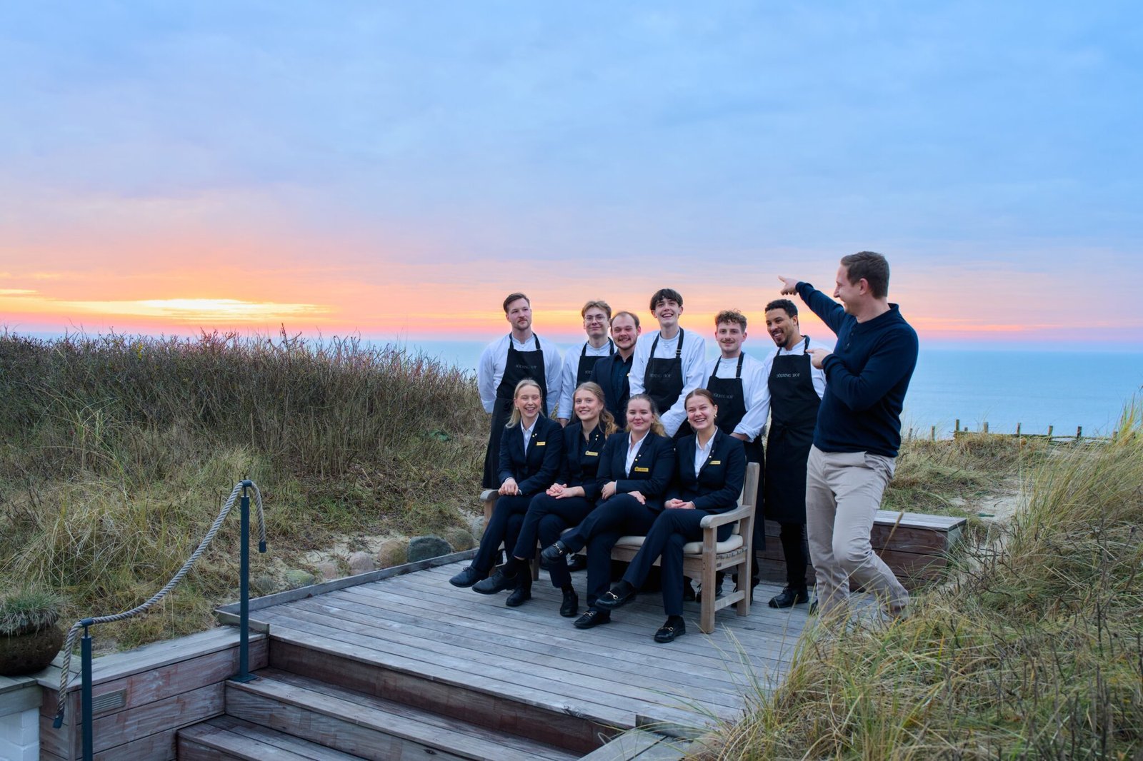 Zehn Personen an Deck bei Sonnenuntergang, die meisten in schwarzen Uniformen.