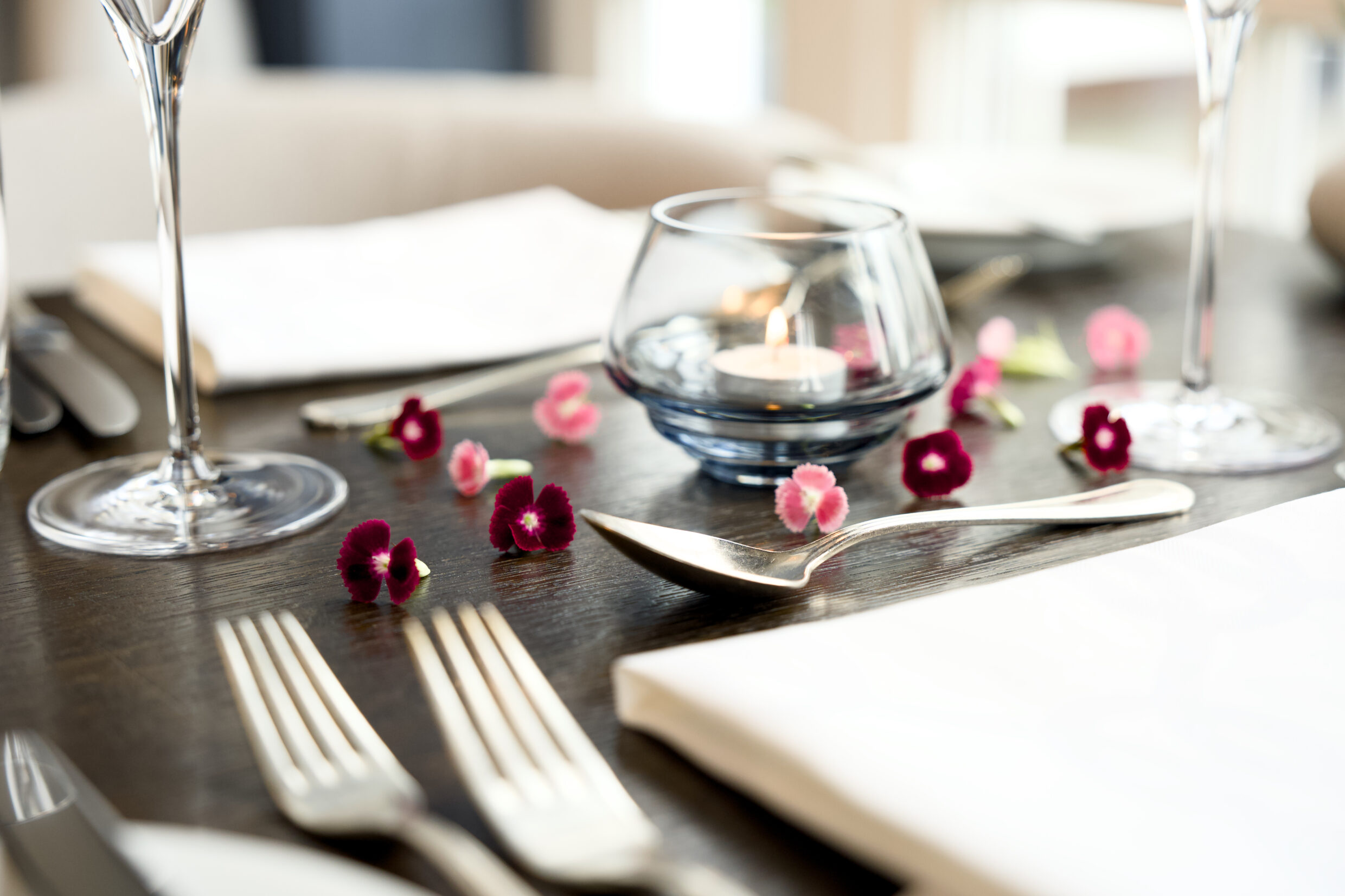 Romantischer Restauranttisch mit Besteck, Servietten, Blütenblättern und Kerzenständer.