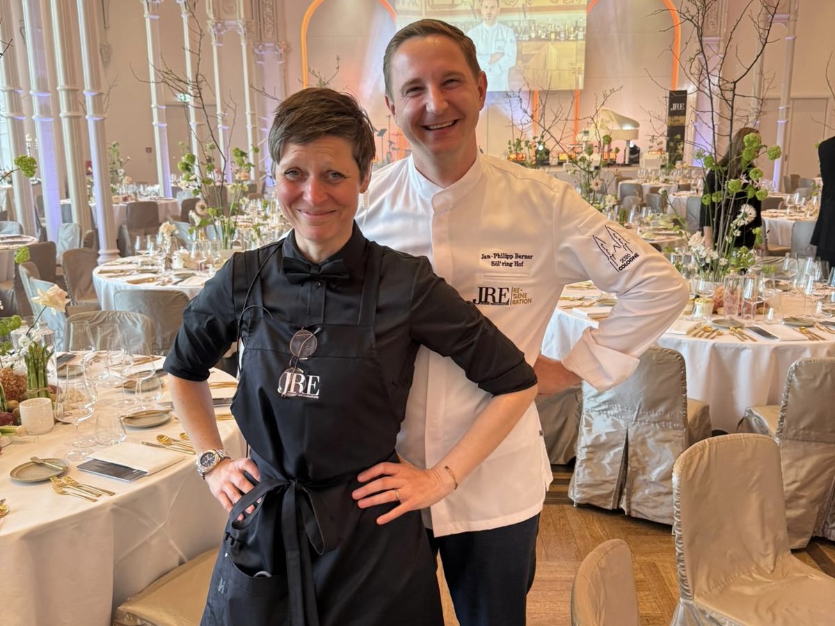 Smiling chefs pose in elegant dining hall with event tables.
