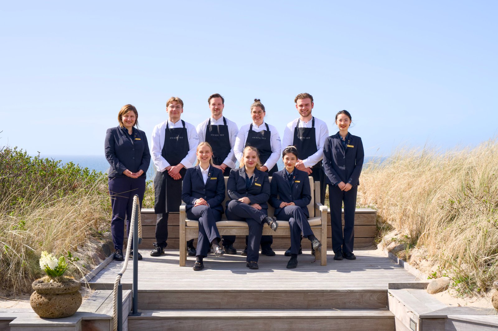 Eight people in uniforms smile for a group photo outdoors.