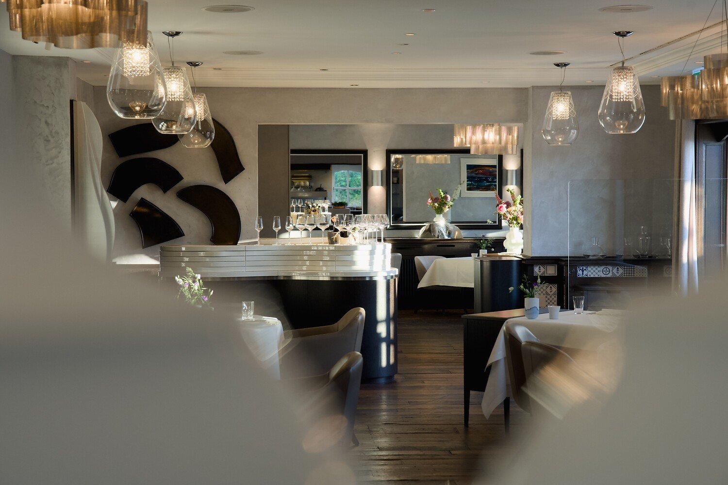 Modern restaurant with set tables, art displays, soft light, windows.