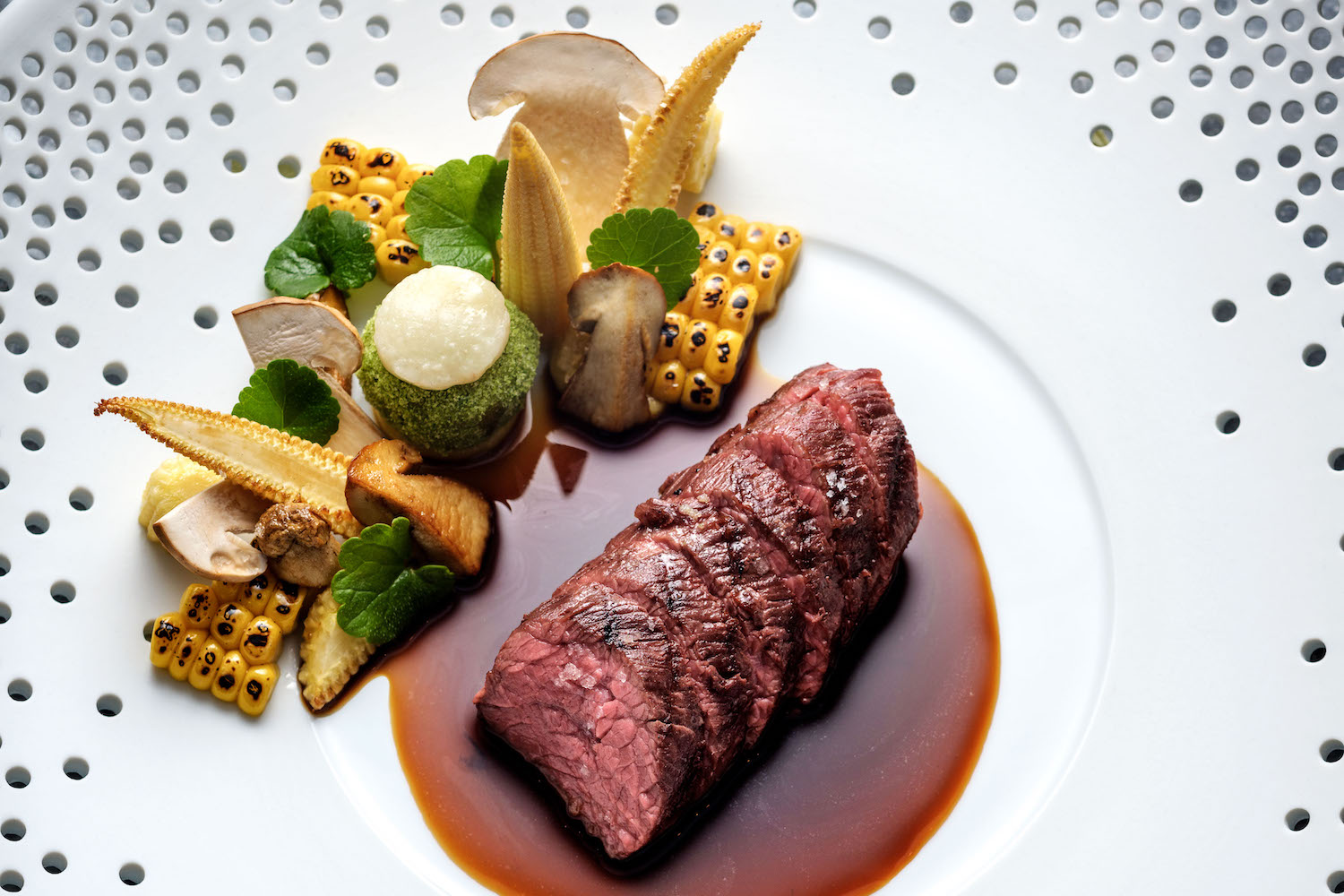 In Scheiben geschnittenes, angebratenes Steak mit brauner Soße, Mais, Pilzen und Gemüse.