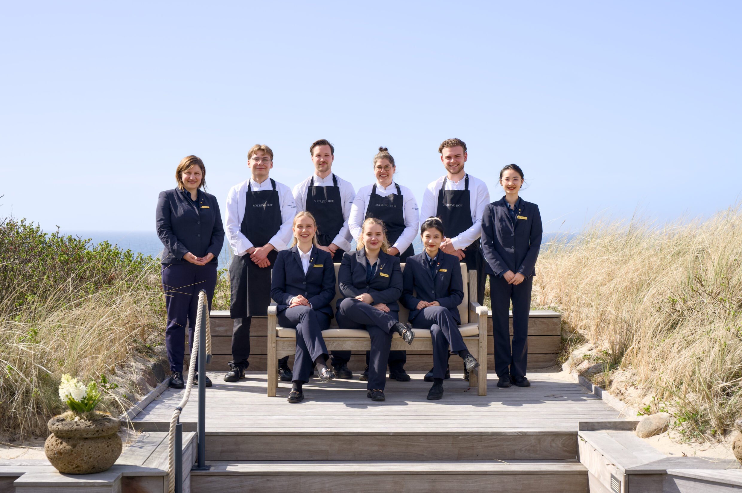 Eight uniformed people pose outdoors on wooden steps, clear sky.