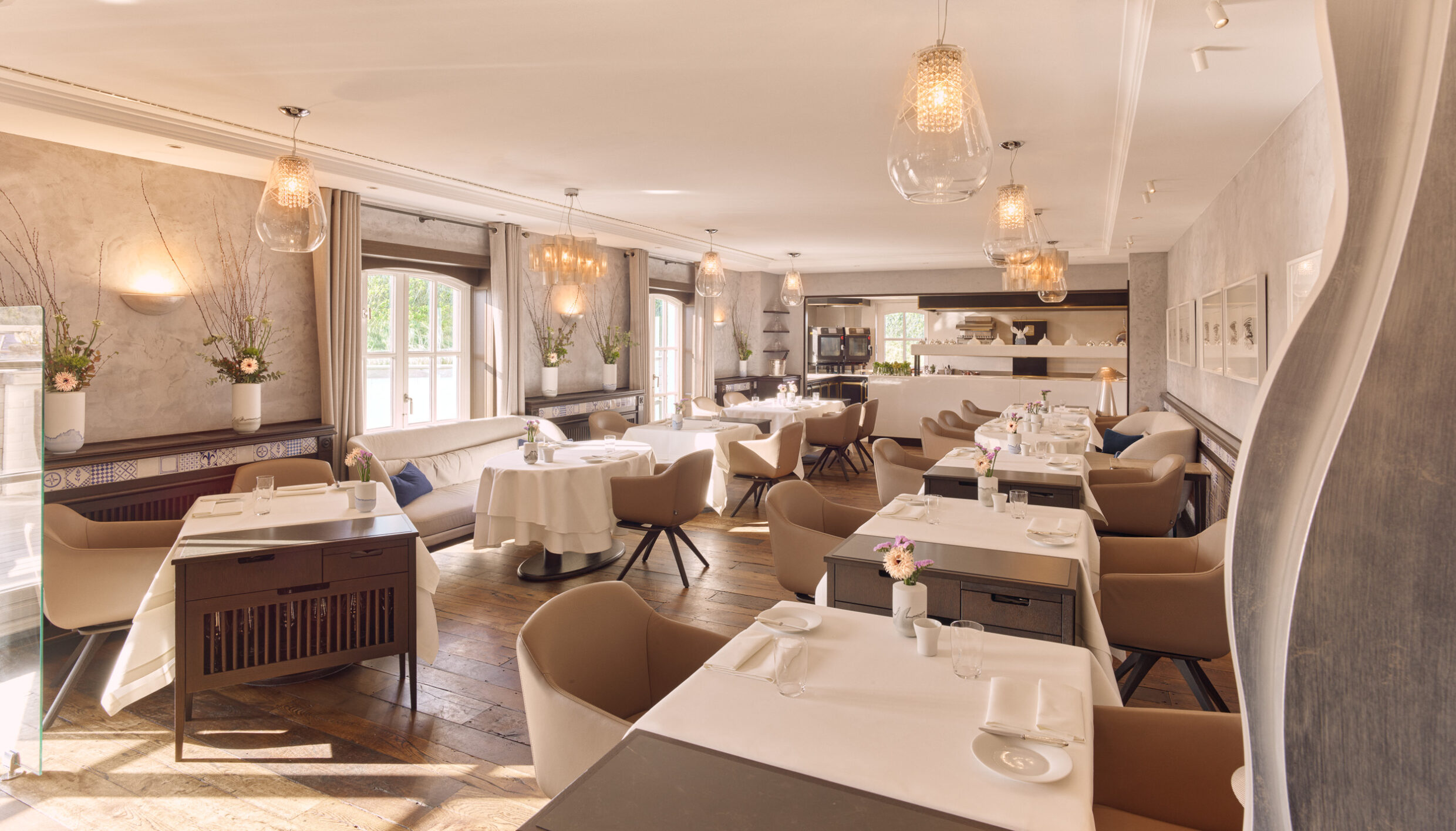 Helles, elegantes Esszimmer mit gedeckten Tischen, beigen Stühlen und Blumen.