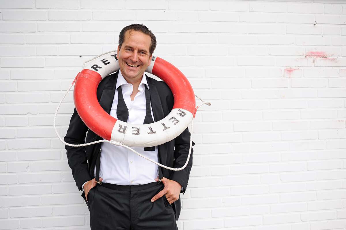 Lächelnder Mann im Anzug mit einer Rettungsboje um den Hals, Backsteinmauer.