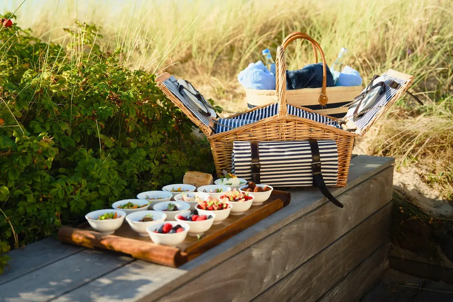 Ein offener Picknickkorb auf einer Bank, blaue Handtücher, Snacks in der Nähe.