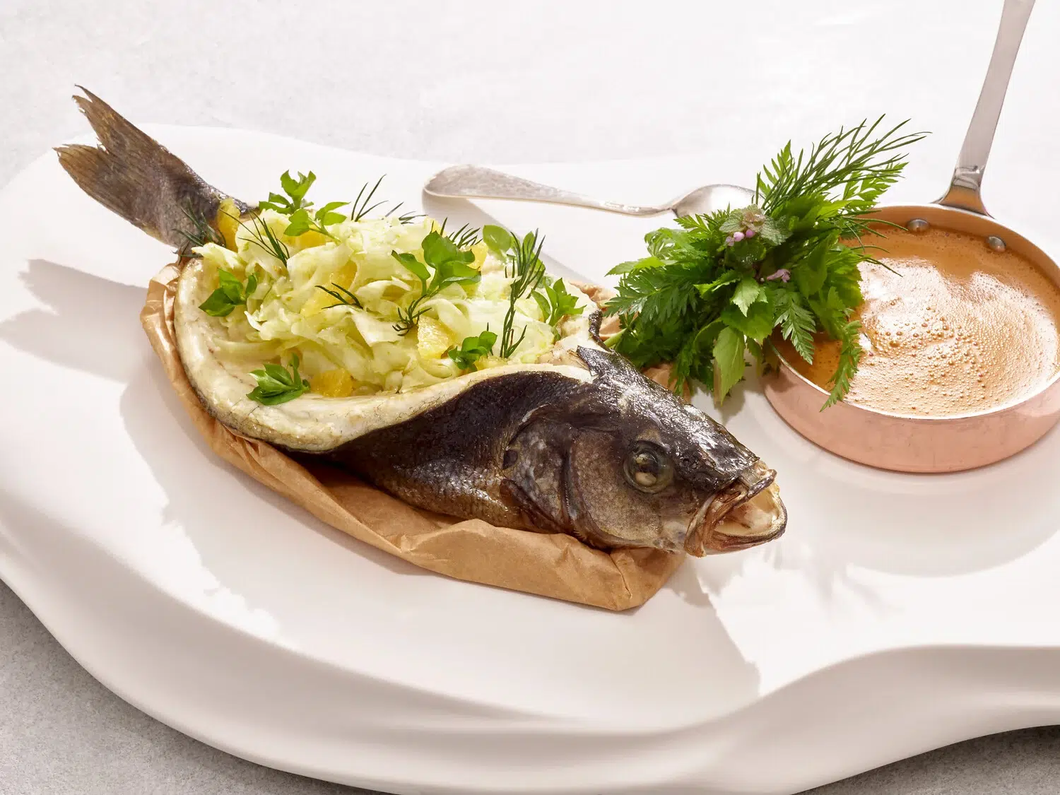Gekochter Fisch mit Gemüse und cremiger Soße auf einem mit Backpapier ausgelegten Teller.